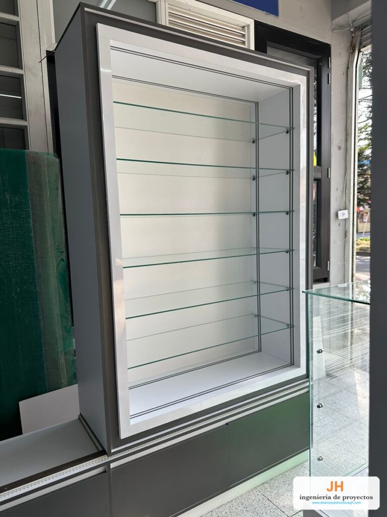 Vitrina panorámica de pared en gris y blanco con seis entrepaños de vidrio templado y bodega en la base, local en Bogotá, obra de JH