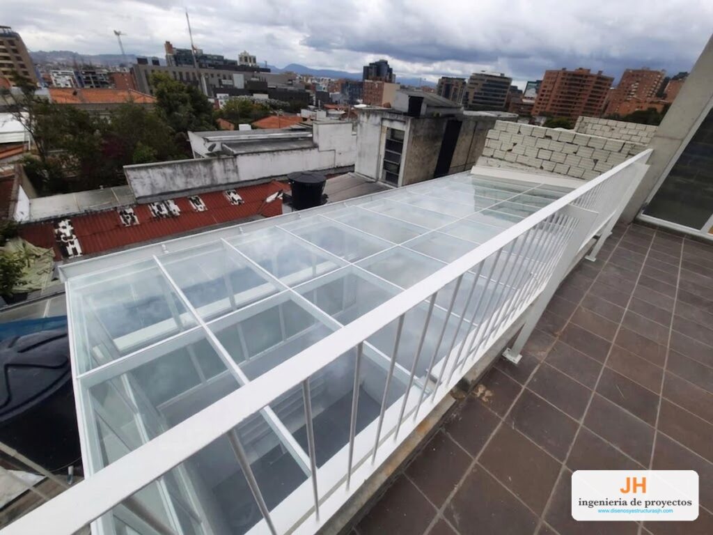 Cubierta de patio interior en vidrio laminado sobre estructura de acero cold rolled pintado blanco, vista desde la terraza de un edificio en Bogotá, obra de JH