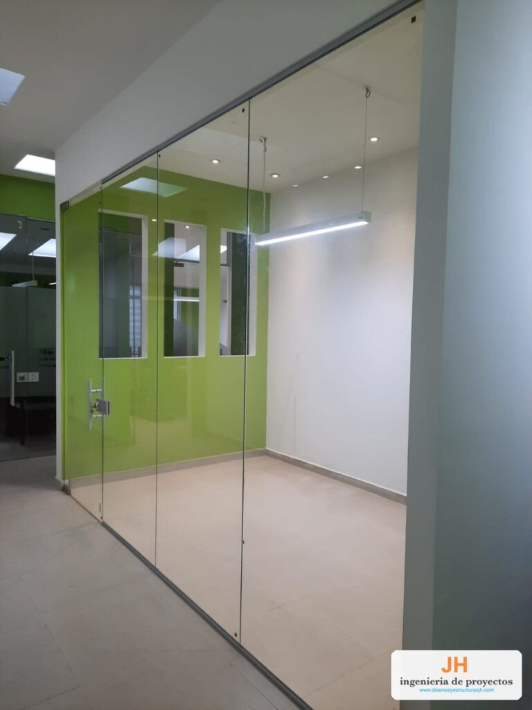 División de oficina en vidrio templado de piso a techo con puerta de vidrio y herrajes en acero inoxidable, oficinas en Bogotá, obra de JH