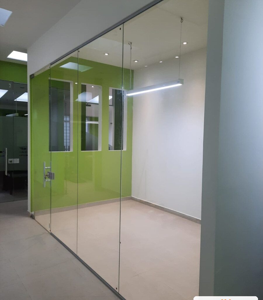 División de oficina en vidrio templado de piso a techo con puerta de vidrio y herrajes en acero inoxidable, oficinas en Bogotá, obra de JH