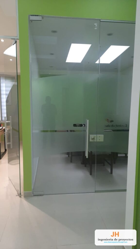 Puerta batiente en vidrio templado con franja esmerilada, manija tubular y chapa en acero inoxidable, sala de juntas en Bogotá, obra de JH