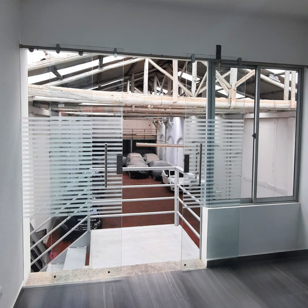 Puerta en vidrio templado deslizante con sistema ITA-K4 en acero inoxidable, diseño moderno y resistente para interiores y oficinas.