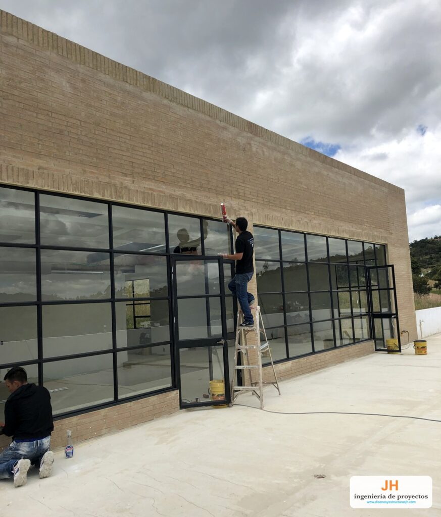 Fachada flotante en aluminio negro y vidrio en instalación, obra JH